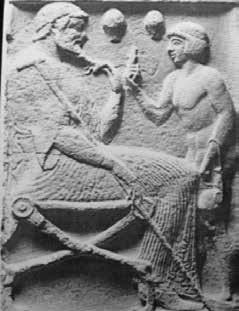 Fig 2: Late 6th or early 5th century BC tombstone showing a physician and his patient or student. The physician is seated on a folding stool holding his staff and stroking his beard; the boy (much restored) carries an aryballos of oil or, as Wickkiser (2008:16) interprets, hanging cupping vessels. Two cups are shown between the figures. Such cups were made of bronze, and after being heated were applied either to divert humours away from a site or attract them to it. (Phillips, Plate 8,1973)